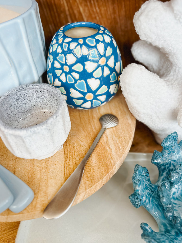 Decorative items including a blue ceramic vase with floral patterns, a silver nautilus cheese spreader, and coral-like sculptures on a wooden surface.