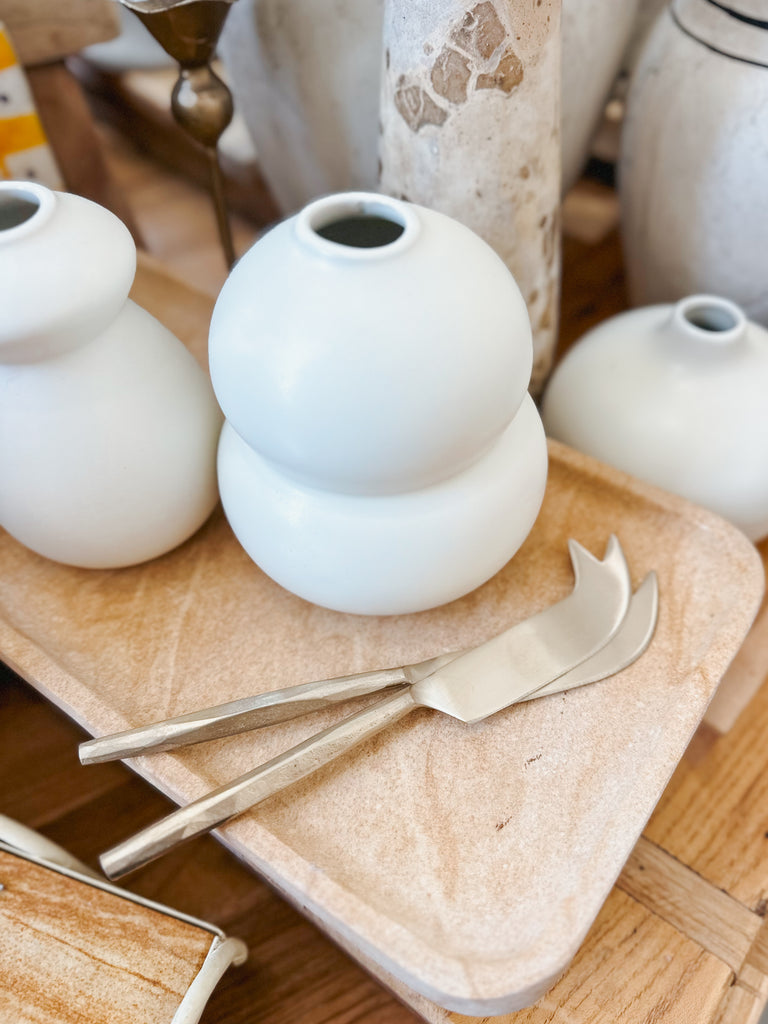 White ceramic vases on a wooden surface with cheese knives.